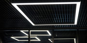 Modern office lighting. Thin lamps in office dark ceiling. LED white cold light over workplaces.